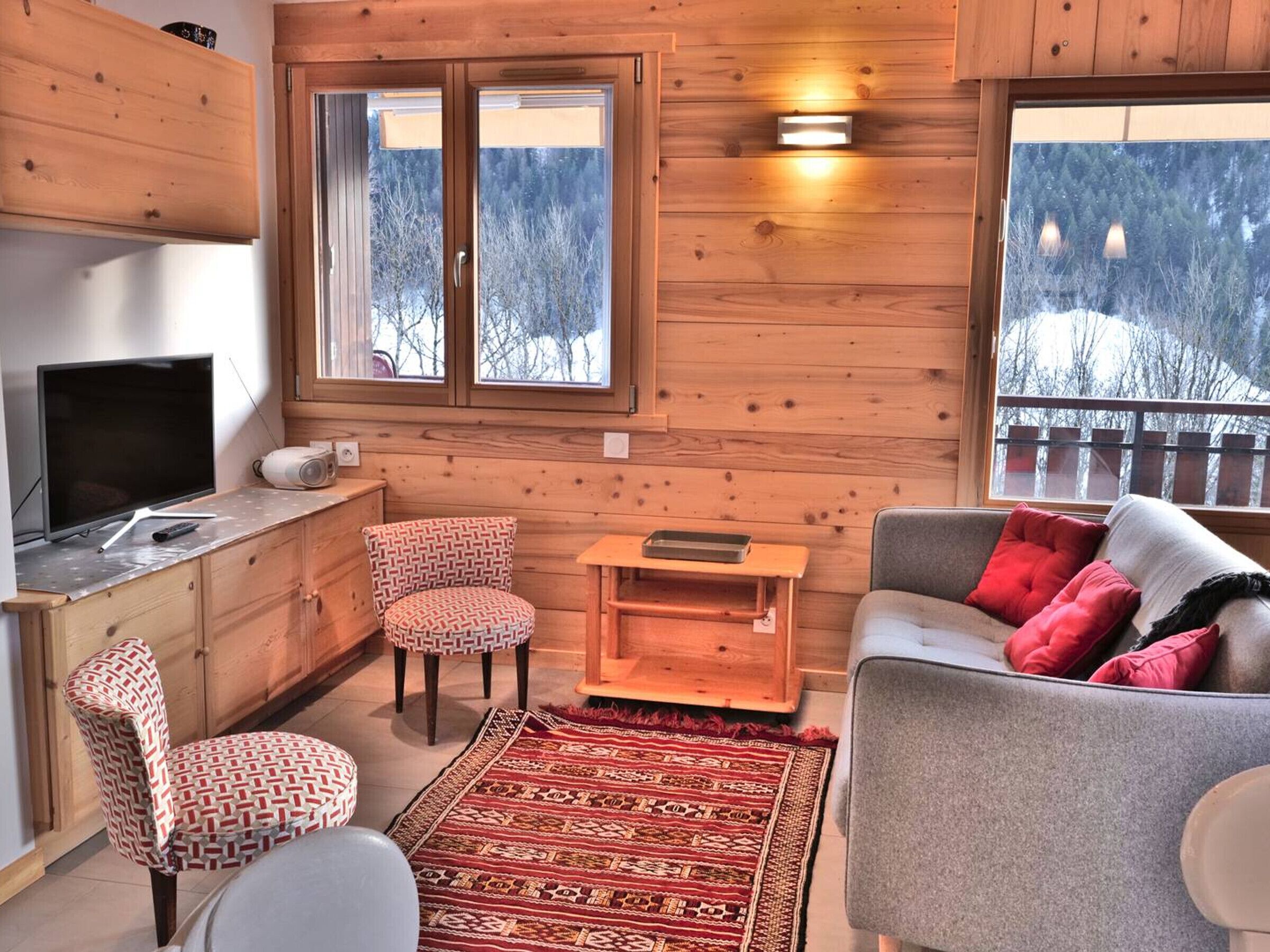 A cozy cabin interior with a wooden interior, a sofa, a chair, a television, and a window with a view of trees.