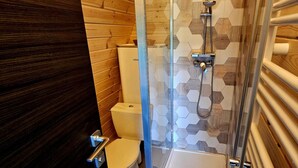 A modern bathroom with a glass-enclosed shower, a toilet, and a wooden wall.