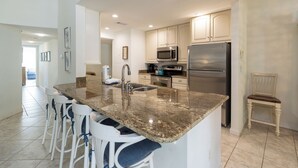 A kitchen with granite countertops, stainless steel appliances, and white cabinetry. There are bar stools and a chair near the kitchen island. - 1690 Bluff Villas: 3 Bds, Next to South Beach Marina, Free Bikes (Hilton Head Island)