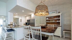 A modern kitchen with white cabinetry, a central island with bar stools, a hanging light fixture, and a dining area with white chairs. - 1690 Bluff Villas: 3 Bds, Next to South Beach Marina, Free Bikes (Hilton Head Island)