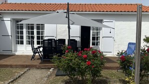 Un pati amb mobiliari exterior, un edifici blanc amb teulada enrajolada i un jardí amb flors vermelles.