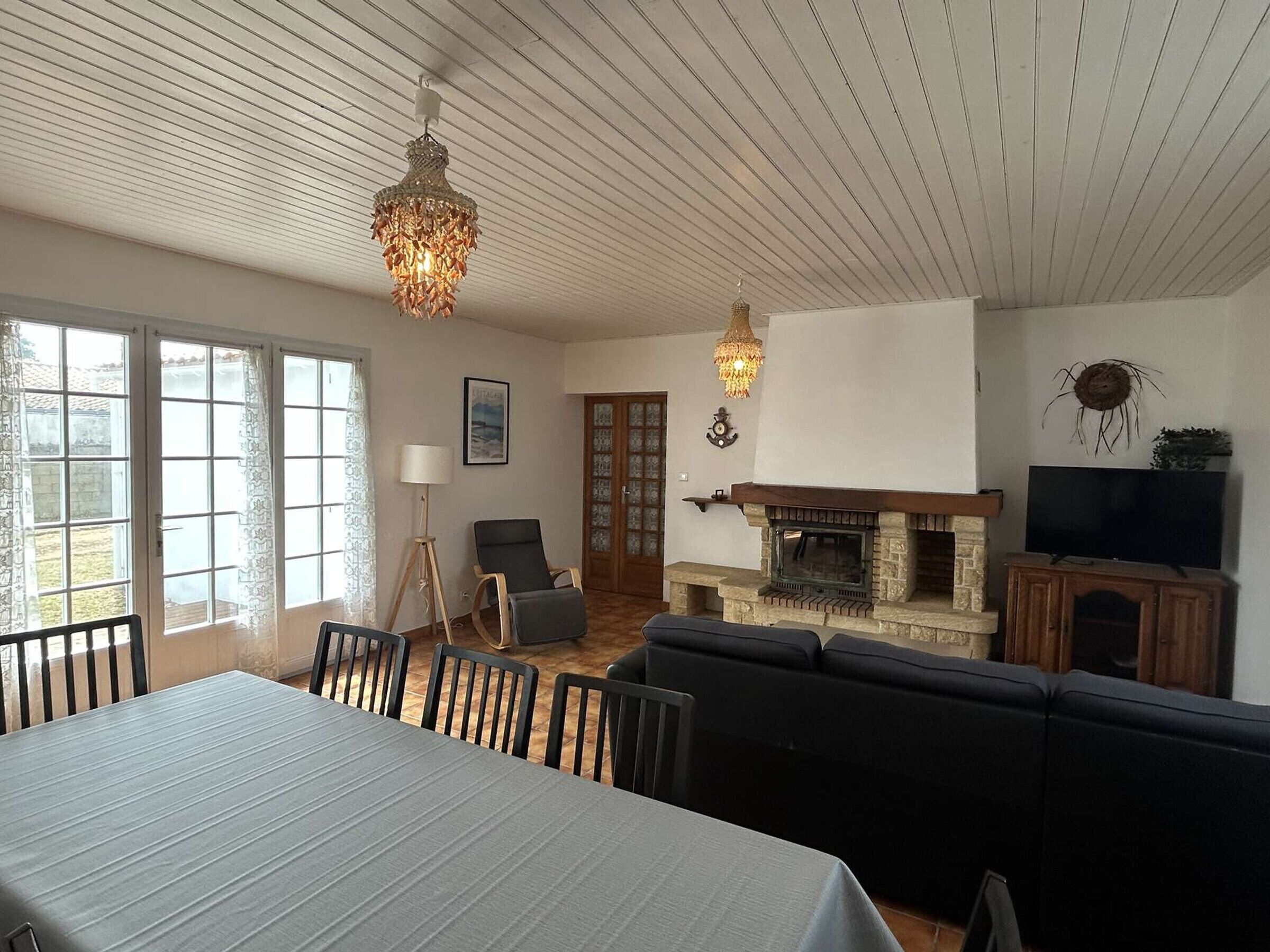 En rummelig stue med pejs, et spiseområde med bord og stole, samt en siddeplads med sofaer.