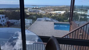 Une vue depuis un balcon donnant sur une piscine, avec en arrière-plan un paysage urbain composé d’immeubles et d’un ciel dégagé.