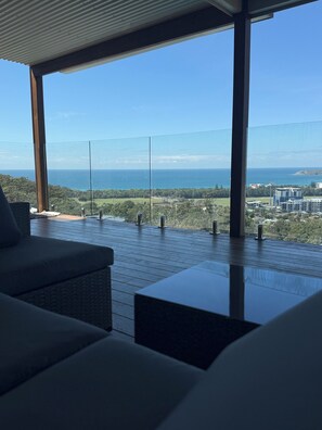 A modern outdoor seating area with a view of the ocean and distant buildings. - Hilltop Family Oasis w/ Pool & Endless Ocean Views (Coffs Harbour)