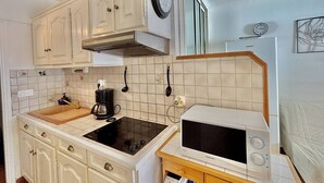 Kompakti keittiö, jossa on valkoiset kaapit, musta liesi, mikroaaltouuni ja kahvinkeitin.