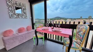 A balcony with a pink table set for two, a cushioned bench, and chairs with floral upholstery. - Studio with pool access in Cap d'Agde (Cap d'Agde)