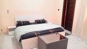 Un dormitorio con cama, mesitas de noche y un otoman para guardar objetos.