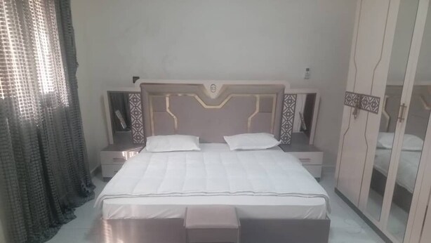 Un dormitorio ordenado con una cama grande, mesitas de noche, un banco y un armario.