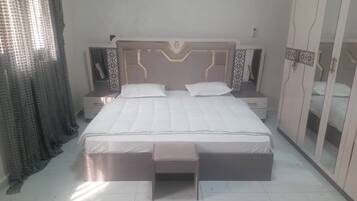 A neatly arranged bedroom with a large bed, bedside tables, a bench, and a wardrobe.