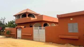 A two-story building with a flat roof and a red facade. There are two large gates and a small window with shutters.