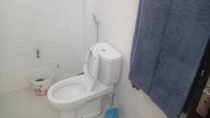 Un baño con un inodoro, un cubo azul de limpieza y una toalla colgada en la pared.