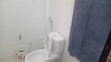A bathroom with a toilet, a blue cleaning bucket, and a towel hanging on the wall.