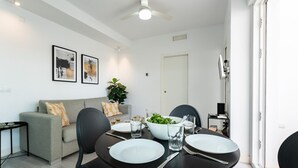 Un comedor moderno con una mesa redonda, sillas negras y un sofá gris. Hay dos obras de arte enmarcadas en la pared, un ventilador de techo y una puerta que conduce a otra habitación.