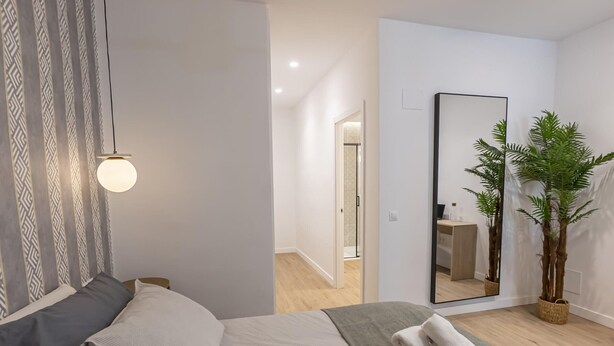 Un dormitorio moderno con una cama, un espejo y una planta en maceta.