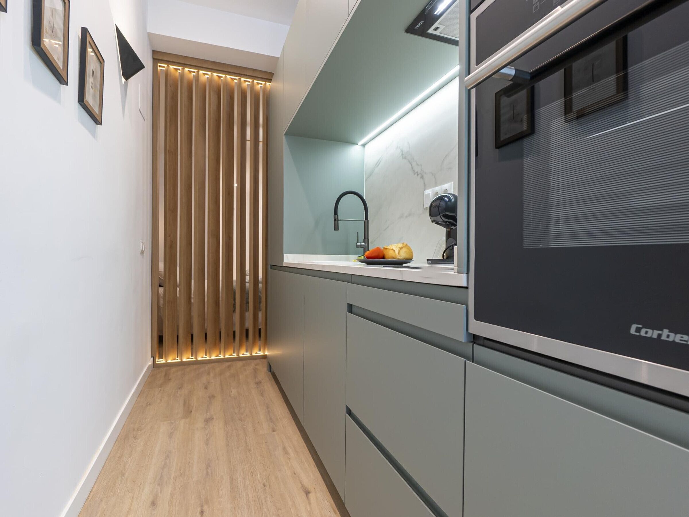 A modern kitchen with a built-in oven, a marble backsplash, and a wooden divider.