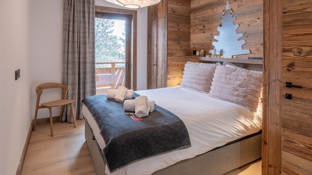 A bedroom with a bed, a wooden headboard, a nightstand, a chair, and a window with curtains. - Luxury apartment, Alpe d'Huez center (Huez)