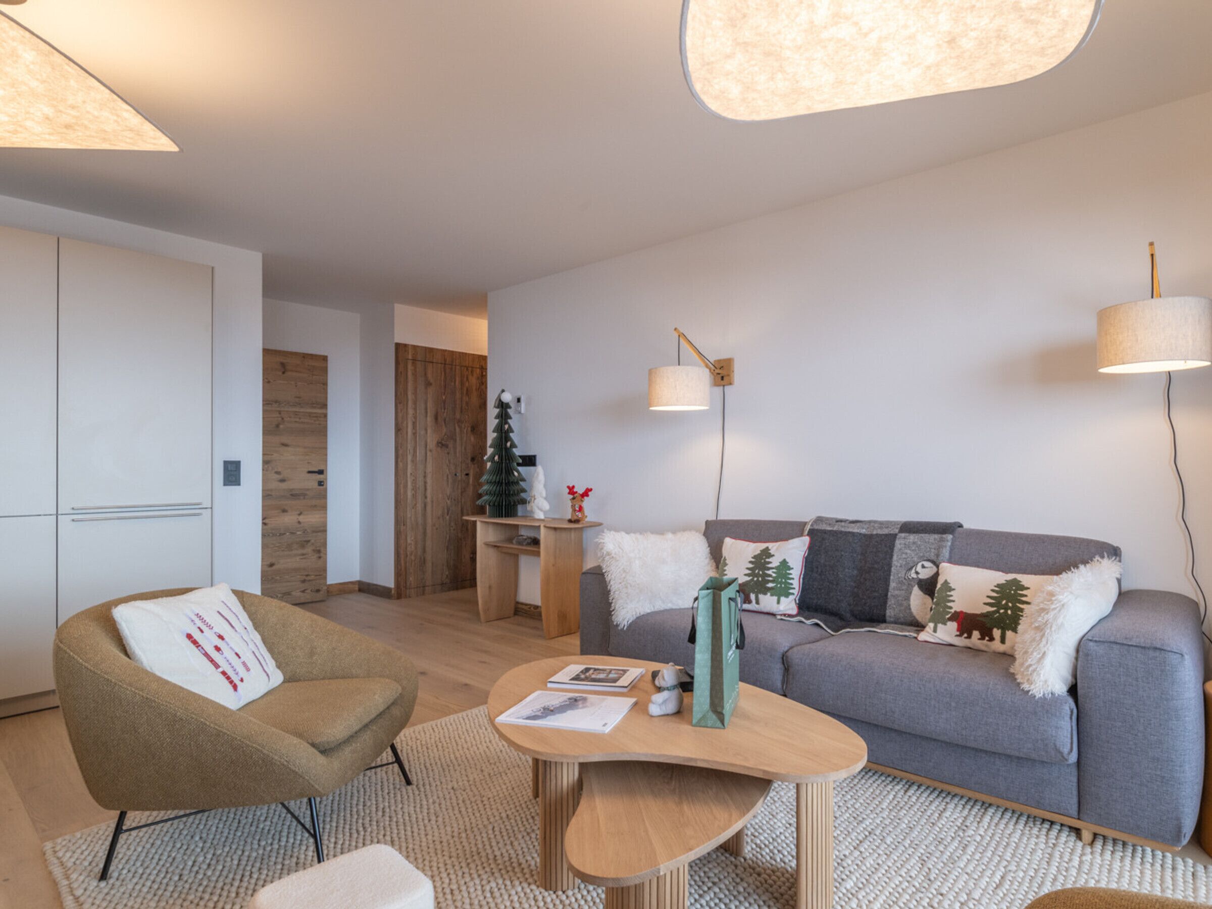 Ett modernt vardagsrum med en grå soffa, en brun fåtölj och ett träbord. Där finns också ett litet träbord med en julgran och en lampa.