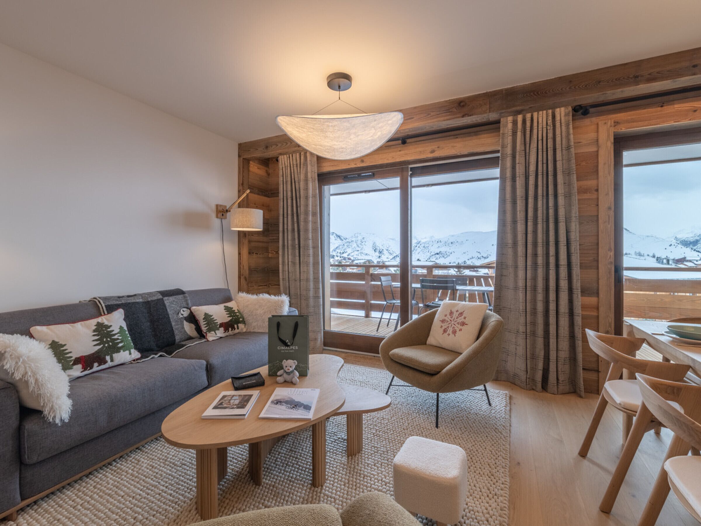 Een knusse woonkamer met een bank, fauteuil, salontafel en uitzicht op besneeuwde bergen door grote ramen.