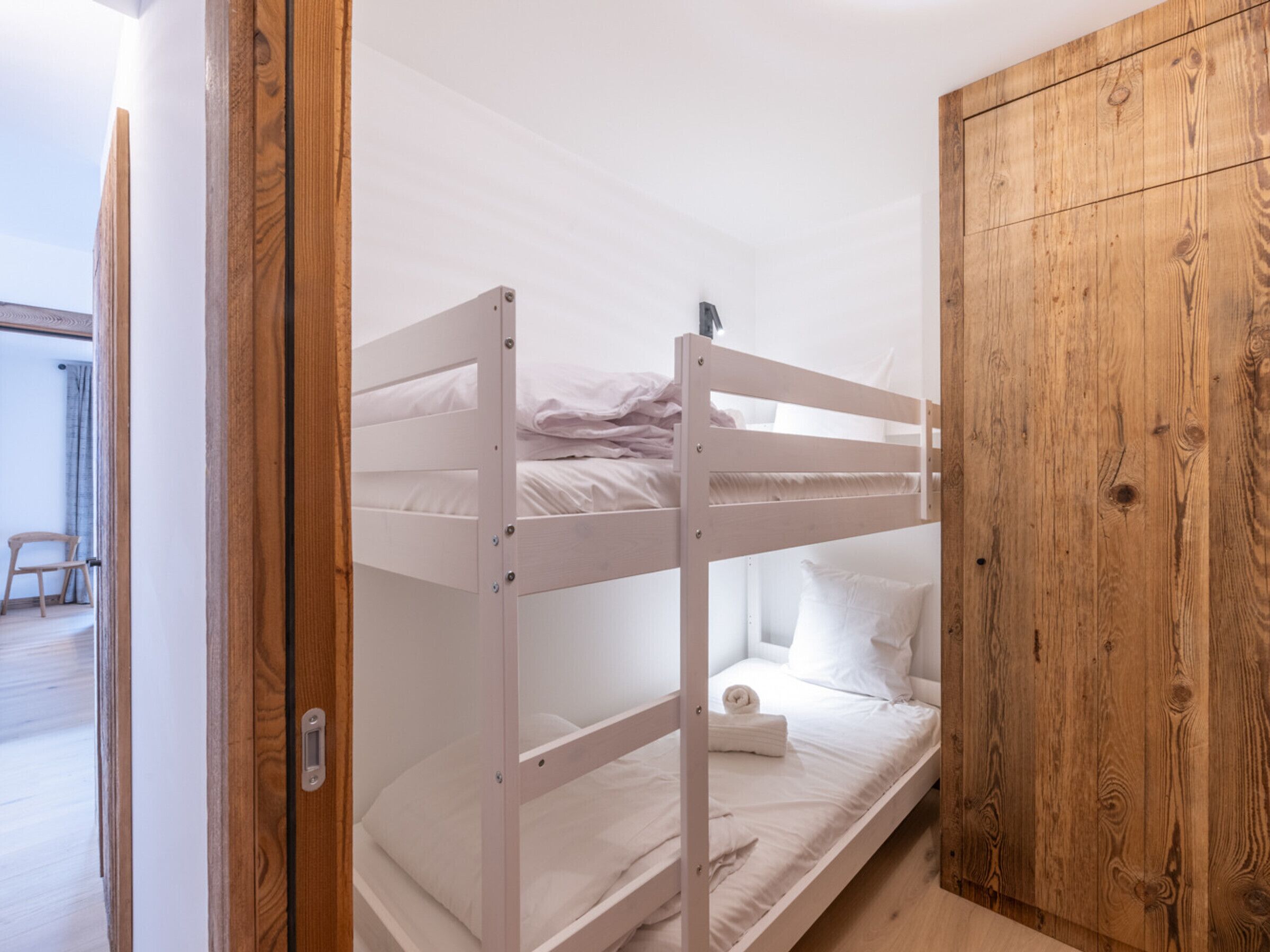Une chambre avec des lits superposés, une armoire en bois et une porte donnant sur une autre pièce.