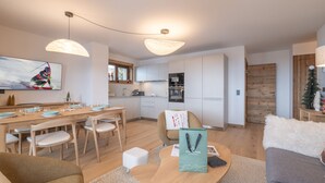 A modern kitchen with white cabinets, a dining area with a wooden table and chairs, and a living room with a sofa and a coffee table. - Luxury apartment, Alpe d'Huez center (Huez)