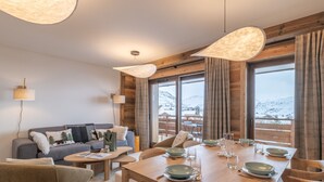 A dining area with a wooden table set for four, surrounded by wooden chairs. There is a sofa with cushions and a lamp in the background. - Luxury apartment, Alpe d'Huez center (Huez)