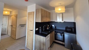 Una cocina compacta con armarios de madera, encimera negra, un lavabo, una estufa y un microondas.
