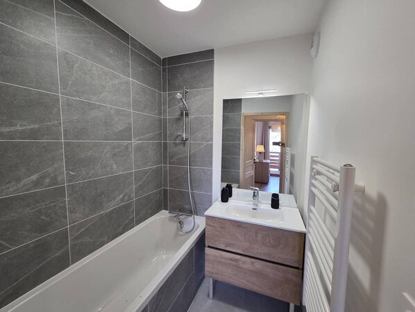 Une salle de bain moderne équipée d’une baignoire, d’une douche et d’un meuble-lavabo avec un miroir.