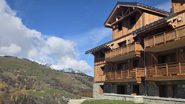 Un edificio de madera de varios pisos con balcones, frente a un paisaje montañoso.