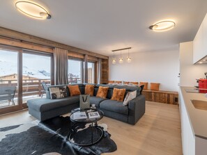 Ein modernes Wohnzimmer mit einer Couch, einem Glastisch und Blick auf verschneite Berge.