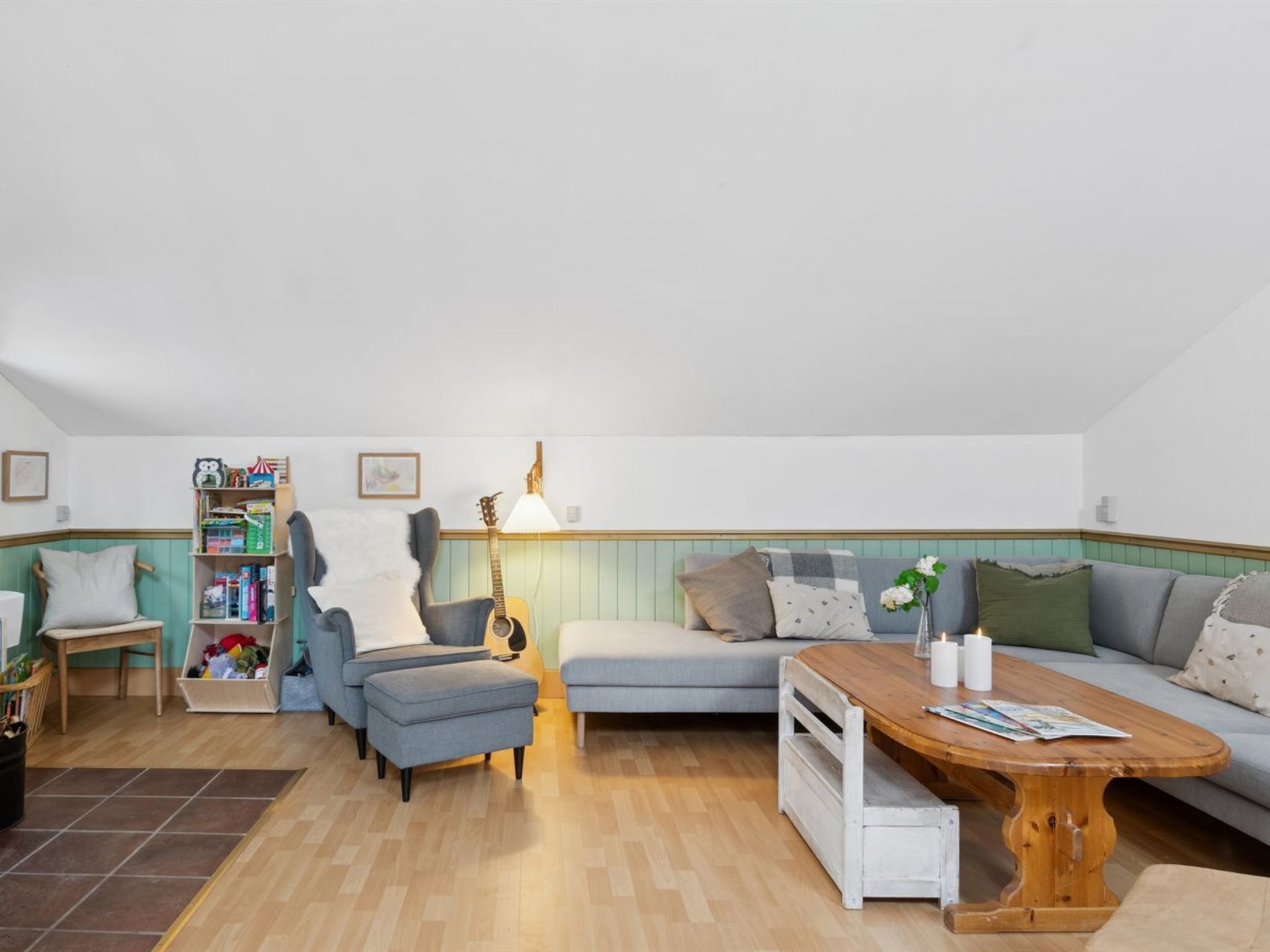Ein gemütliches Wohnzimmer mit Sofa, Hocker, Couchtisch, Bücherregal und einer Gitarre.