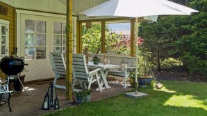 En overdækket terrasse med udendørs møbler, grill og plantekasser.