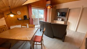 Une cuisine compacte avec un coin repas, des murs en bois, une fenêtre avec des rideaux et un luminaire au plafond.