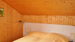 Une pièce aux murs lambrés, comprenant un lit, une table de chevet et une lampe fixée au mur.