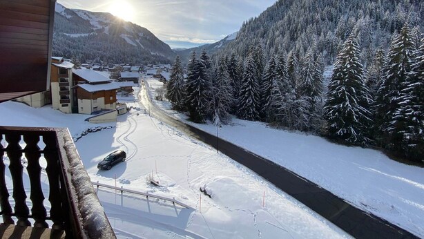 Un paysage montagneux enneigé, avec une route et des bâtiments au premier plan.