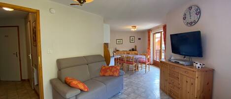 Ein Wohnzimmer mit einer Couch, einem Fernseher, einem Holzschrank und einem Essbereich.