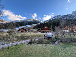 Un chalet de montagne composé de plusieurs bâtiments en bois, un ciel dégagé et des collines enneigées en arrière-plan.