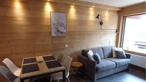 A modern living room with a wooden wall, a grey sofa, a wooden coffee table, and a framed picture. - Renovated studio for 4 with balcony in Grand-Bornand (Le Grand-Bornand)