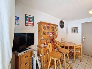 Un salon équipé d’un téléviseur à écran plat, de meubles en bois, d’une table à manger avec des chaises et d’une horloge murale.