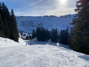 Une pente de montagne enneigée, avec des skieurs et un ciel dégagé.