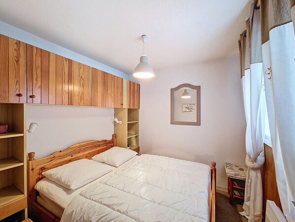 Une chambre avec une tête de lit en bois, un lit avec une literie blanche, une lampe de chevet, une étagère et un tableau encadré au mur.