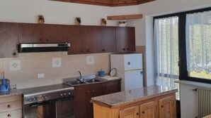 A kitchen with wooden cabinets, a stainless steel stove, a refrigerator, and a window with curtains. - Appartment le Gemme Dolomites escape (Dosoledo)
