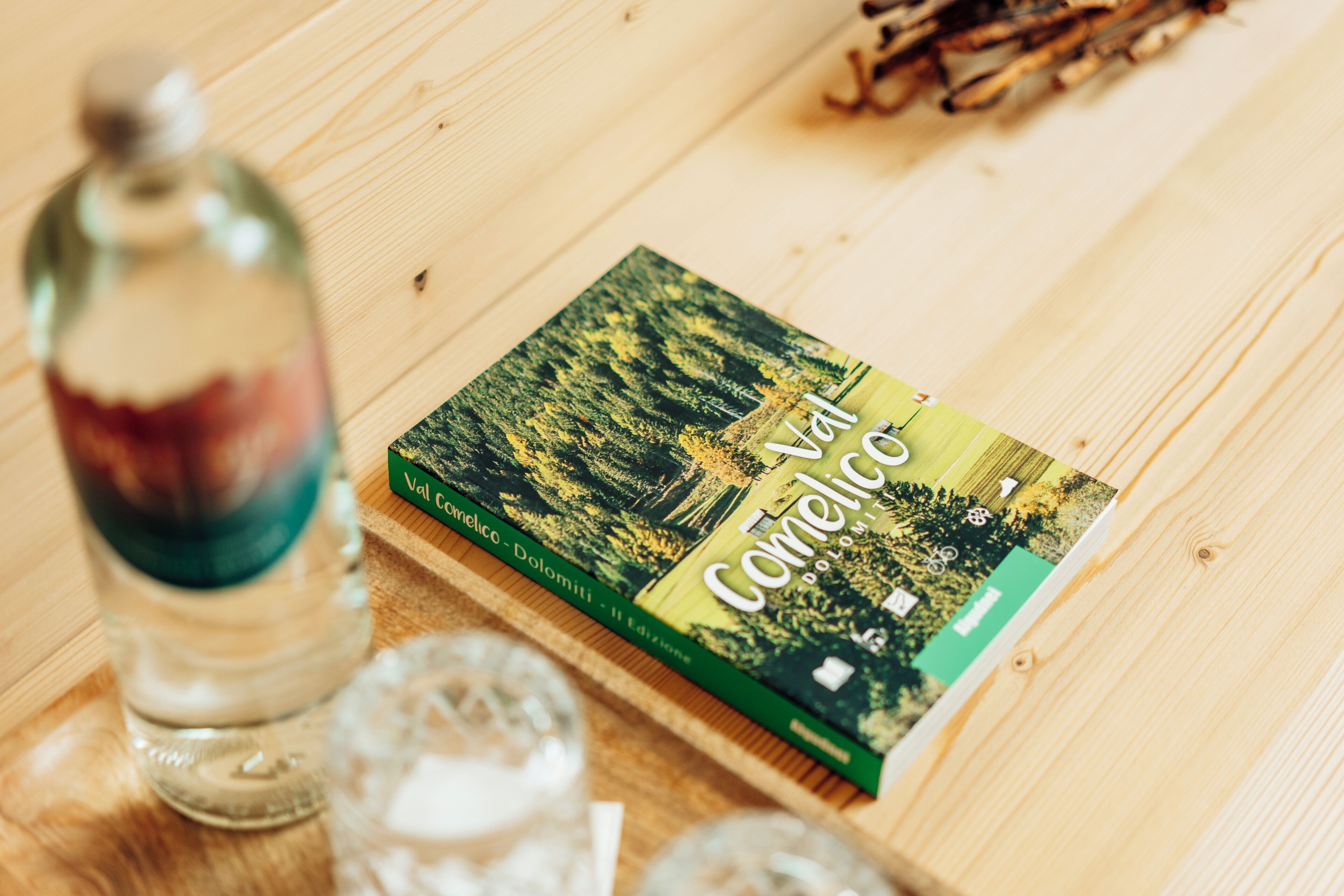 A book titled 'Val Camonica' on a wooden table with a glass bottle and two glasses.