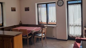 A dining area with a table and chairs, a clock on the wall, and windows with curtains. - Appartment le Gemme Dolomites escape (Dosoledo)