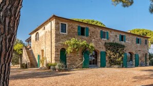 A stone building with green shutters and arched windows, surrounded by trees and a clear sky. - Tenuta San Crescenzio (Toscana)