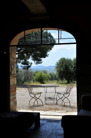An arched doorway leading to an outdoor seating area with two metal chairs and a table, overlooking a landscape with trees and distant mountains. - Tenuta San Crescenzio (Toscana)
