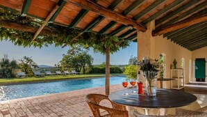 A poolside area with a table, chairs, and a view of a swimming pool and greenery. - Tenuta San Crescenzio (Toscana)