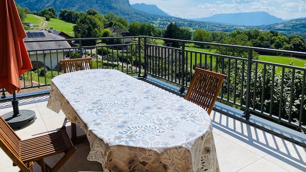 Ein Balkon mit Tisch und Stühlen, mit Blick auf eine reizvolle Landschaft mit Bergen und viel Grün.