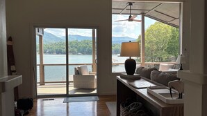 Ein Zimmer mit Seeblick, Deckenventilator, Lampe, Sofa, Tisch mit Laptop und Koffer.