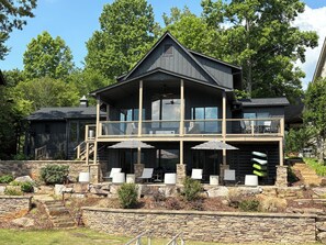 A two-story house with a balcony, stone steps, and outdoor seating. - Still Waters at Lake Chatuge - Private Dock, Hot Tub, Kayaks, SUPs, &  Game Room (Hiawassee)
