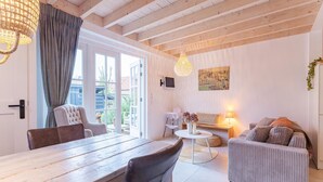 A spacious living area with a wooden dining table, a sofa, and a TV mounted on the wall. - Modern Holiday Home in Vrouwenpolder (Koudekerke)
